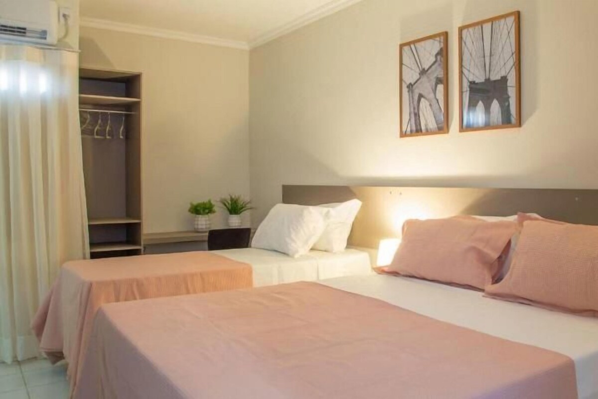 Una habitación de hotel con dos camas, un armario y una mesita con una planta.
