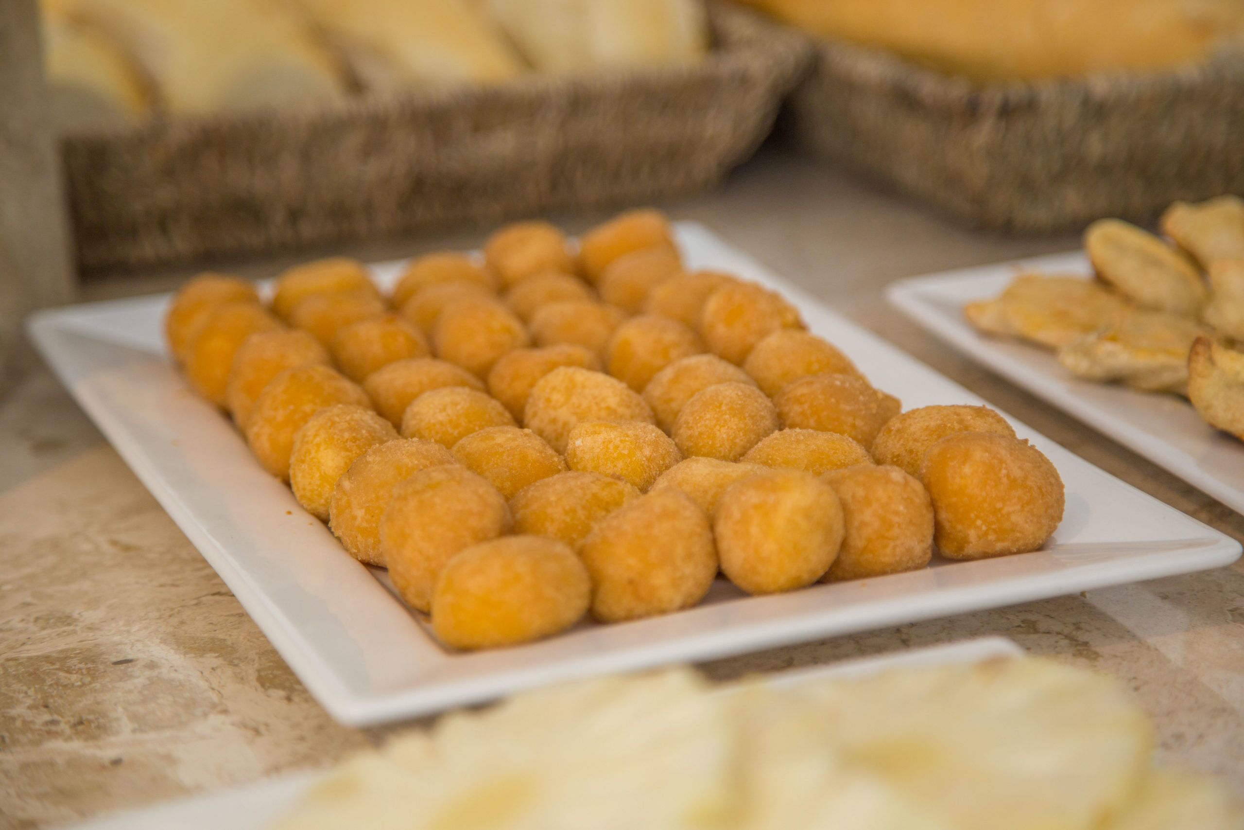 A white rectangular plate with golden-brown fried items, possibly fritters, on a marble countertop.