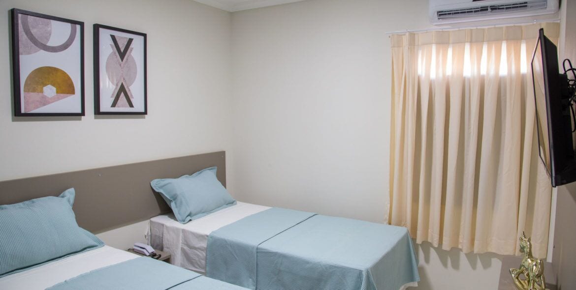 A hotel room with two single beds, a TV, and a window with curtains.