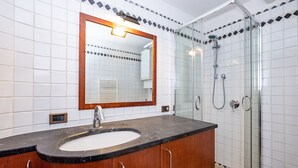A bathroom with a wooden vanity, a sink, a mirror, and a glass shower enclosure.