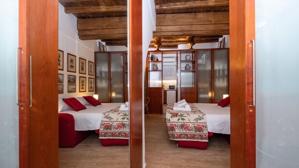 A mirrored room with two beds, wooden ceiling beams, and a small desk with a chair.
