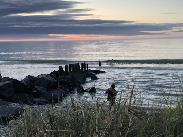 A coastal scene with a rocky shoreline, waves, and a person standing near the water.