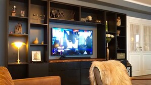 Una sala de estar con un televisor de pantalla plana grande sobre un mueble negro, rodeado de estantes con varios objetos decorativos.
