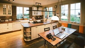 Una cocina moderna con una isla central, armarios blancos y un área de comedor con una computadora portátil y un vaso.