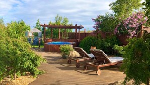 Una terraza de madera con un jacuzzi, dos sillones de relax y una pérgola.