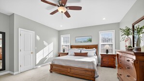 Une chambre à coucher avec un lit en bois, un ventilateur de plafond, une commode et une fenêtre avec des stores.