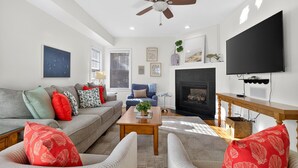 Un salon comprenant un canapé, des fauteuils, une table basse, une cheminée, un téléviseur et un ventilateur de plafond.