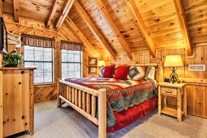 Quarto de cabana de madeira com uma cama, uma mesinha de cabeceira, uma luminária e uma janela com persianas.
