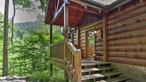 Eine Holzhütte mit einer Veranda und Stufen, die zu einer Tür führen, umgeben von üppiger Vegetation.