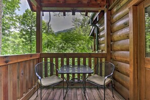 Um deck de madeira com mesa e duas cadeiras, com vista para uma área arborizada.