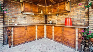 A rustic kitchen with wooden cabinets, a brick wall, and a brick floor.