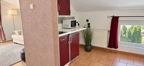 A compact kitchen with a microwave, a red cabinet, a potted plant, and a window with curtains. - Casa Montana - CAPRI apartment with view to the Lake (Balatonalmádi)