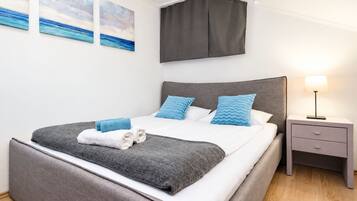 Une chambre moderne avec un grand lit, une literie grise, des coussins bleus et une table de chevet avec une lampe.