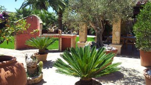 A garden with potted plants, a stone structure, and a patio area. - Holiday home Villa Flumini  (Quartu Sant'Elena)