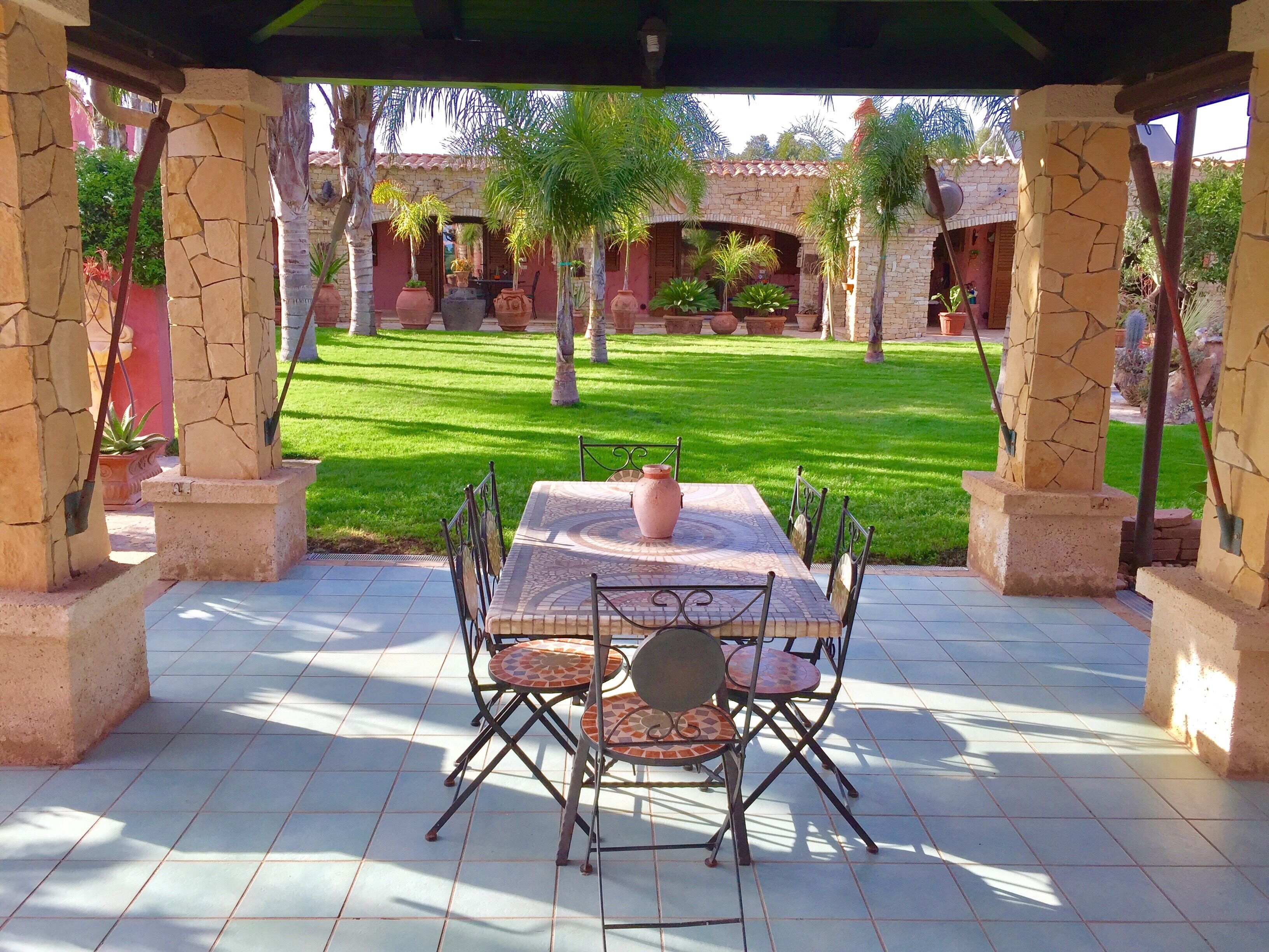 Une terrasse avec une table et des chaises, entourée de piliers en pierre et bordée d’une pelouse bien entretenue.