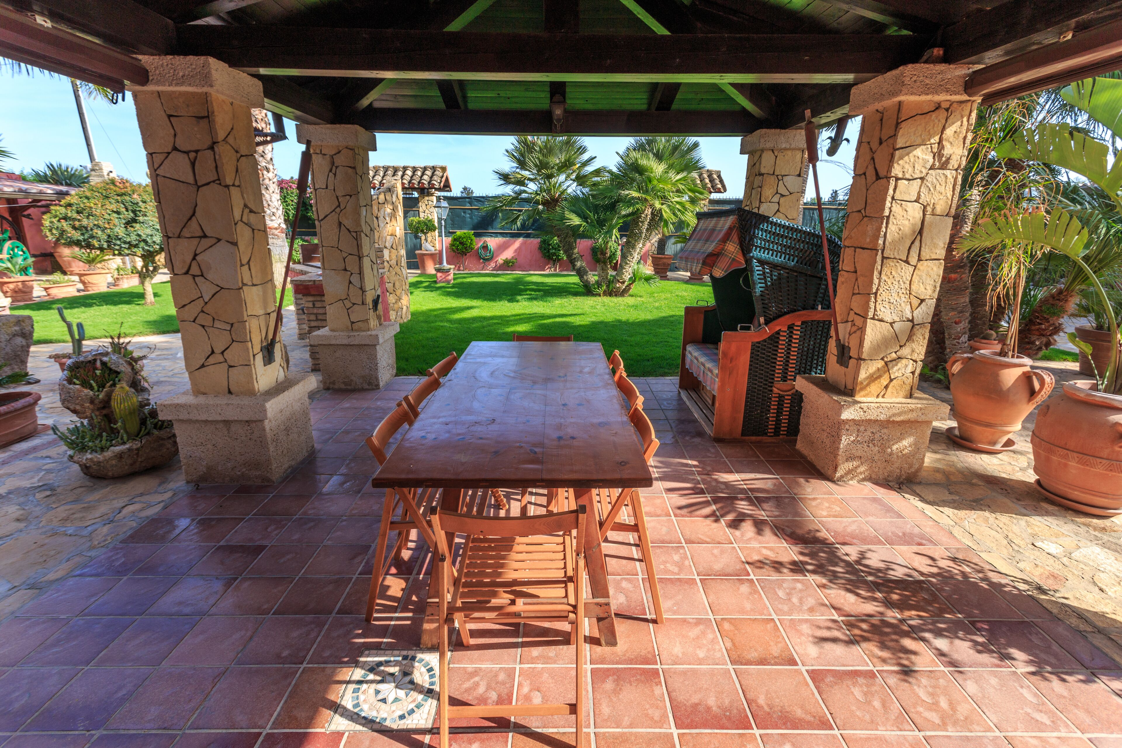 A patio with a wooden table and chairs, stone pillars, and potted plants.