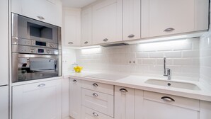 Una cocina moderna con muebles blancos, electrodomésticos de acero inoxidable y encimera blanca.
