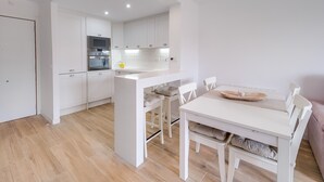 Una cocina moderna con armarios blancos, horno empotrado y un comedor con mesa y sillas blancas.