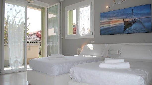 A bedroom with two beds, large windows, and a painting of a sunset over water. - Bnbook-Metropolitan Expo Flat 4 Bilocale con wifi veloce (Rho)