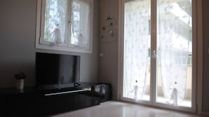 A bedroom with a bed, a TV on a black stand, a potted plant, and a sliding glass door with a view of the outside. - Bnbook-Metropolitan Expo Flat 4 Bilocale con wifi veloce (Rho)