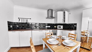 Una cucina moderna con mobili bianchi, una parete di sfondo nera e un tavolo da pranzo in legno apparecchiato con piatti e posate bianche.