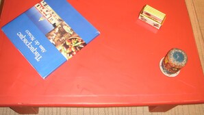 Une table rouge, sur laquelle se trouvent une brochure bleue, une petite pile de livres et un objet décoratif.