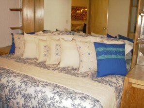 Cama com colcha estampada com flores e várias almofadas.