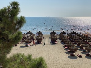 Uma praia com guarda-sóis de palha e espreguiçadeiras, uma faixa de areia e o mar ao fundo.