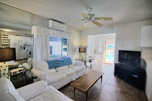 Ein Wohnzimmer mit weißem Sofa, Couchtisch, Fernseher und Deckenventilator.