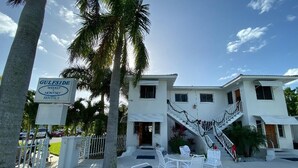 Une propriété située en bord de mer, avec une enseigne indiquant « Gulfside Weekly Rentals », comprenant un bâtiment blanc avec un escalier, des sièges extérieurs et des palmiers.