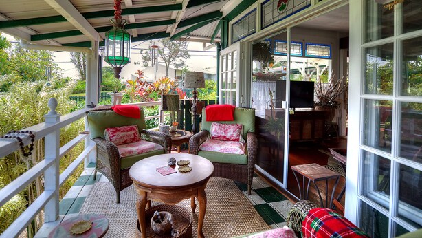 Un porche cubierto con mobiliario de mimbre, una mesa y vista al jardín.