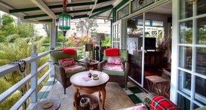 Un porche cubierto con mobiliario de mimbre, una mesa y vista al jardín.