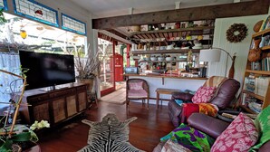 Una sala de estar acogedora con un televisor de pantalla plana, un tapete estampado con diseño de cebra, un sofá de cuero con cojines coloridos y una estantería llena de libros y objetos decorativos.