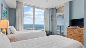 Ein Schlafzimmer mit zwei Betten, einem Fernseher, einem Schminktisch und einem Balkon mit Meerblick.