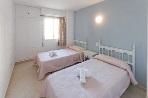 A bedroom with two beds, each with a white headboard and pink bedding. There is a window with floral curtains, a bedside table, and a wardrobe. - PIROPO - Apartment with sea views in Playa de Gandia. (Grau i Platja)