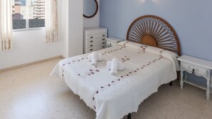 A neatly arranged bedroom with a bed, a bedside table, a dresser, and a window with curtains. - PIROPO - Apartment with sea views in Playa de Gandia. (Grau i Platja)