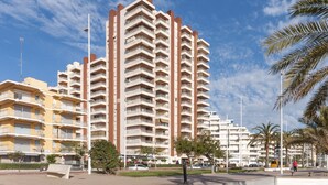 A high-rise residential building with multiple balconies, a pedestrian walkway, and palm trees. - PIROPO - Apartment with sea views in Playa de Gandia. (Grau i Platja)