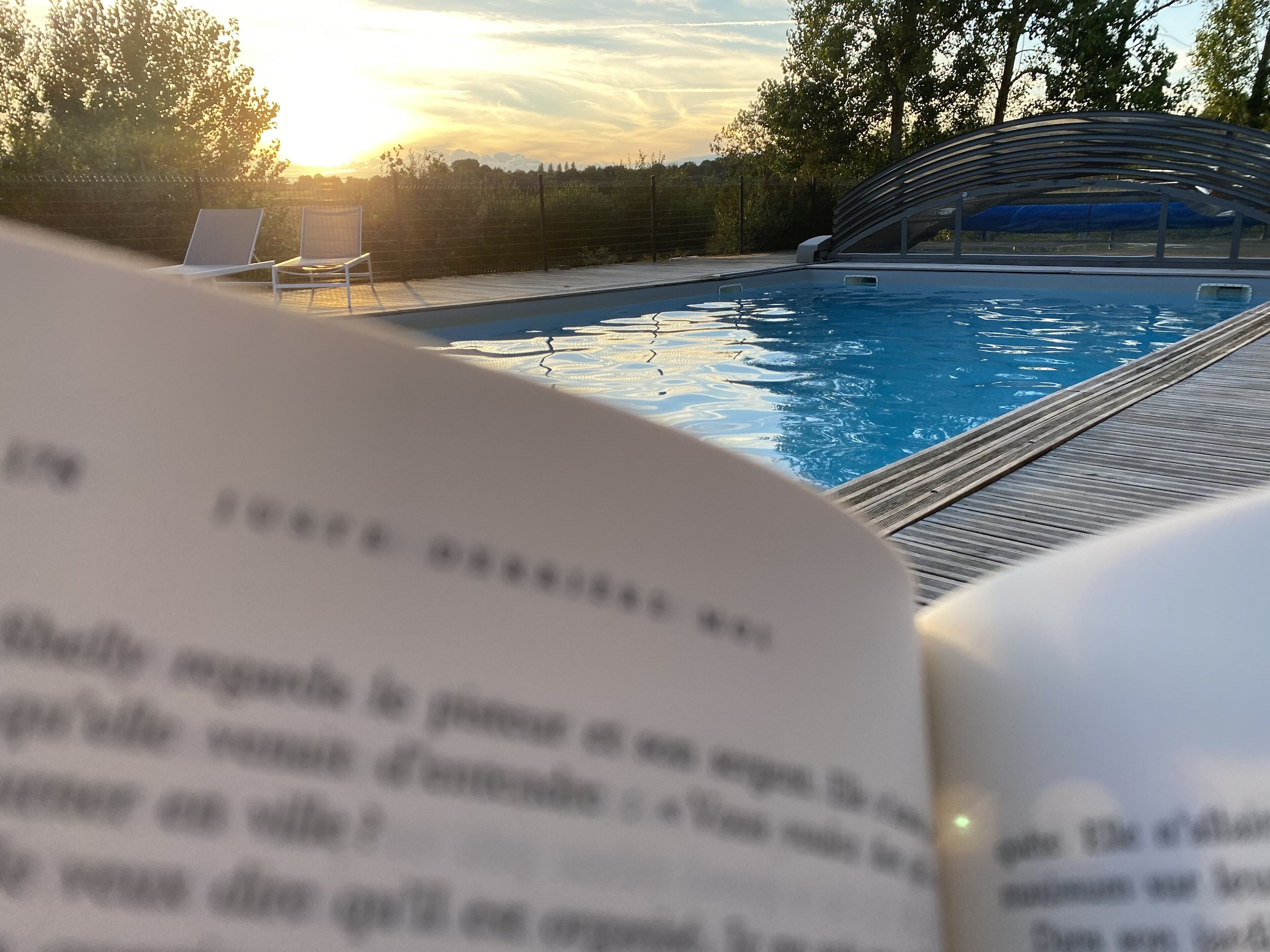 Un libro abierto con vista a una piscina y sillas de descanso.