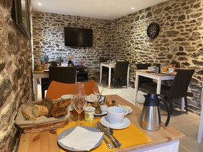 Cenário de café da manhã com paredes de pedra, TV de tela plana e área de refeições rústica.