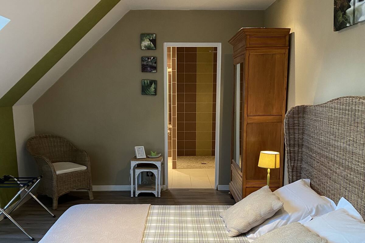 A bedroom with a large bed, a chair, a wardrobe, and a small table.
