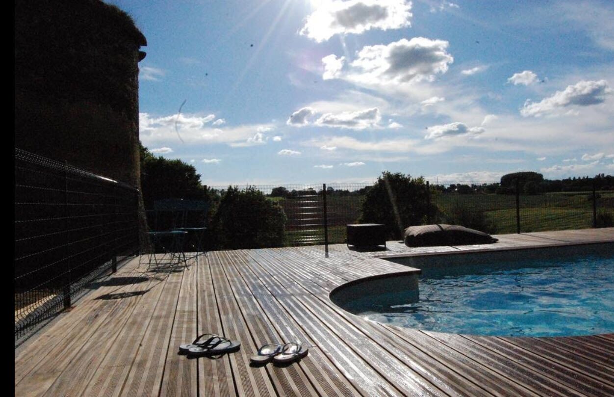 Une terrasse en bois avec une piscine, une clôture en métal et un ciel dégagé.