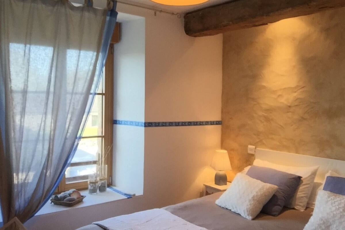 A bedroom with a bed, bedside table, lamp, and a window with curtains.