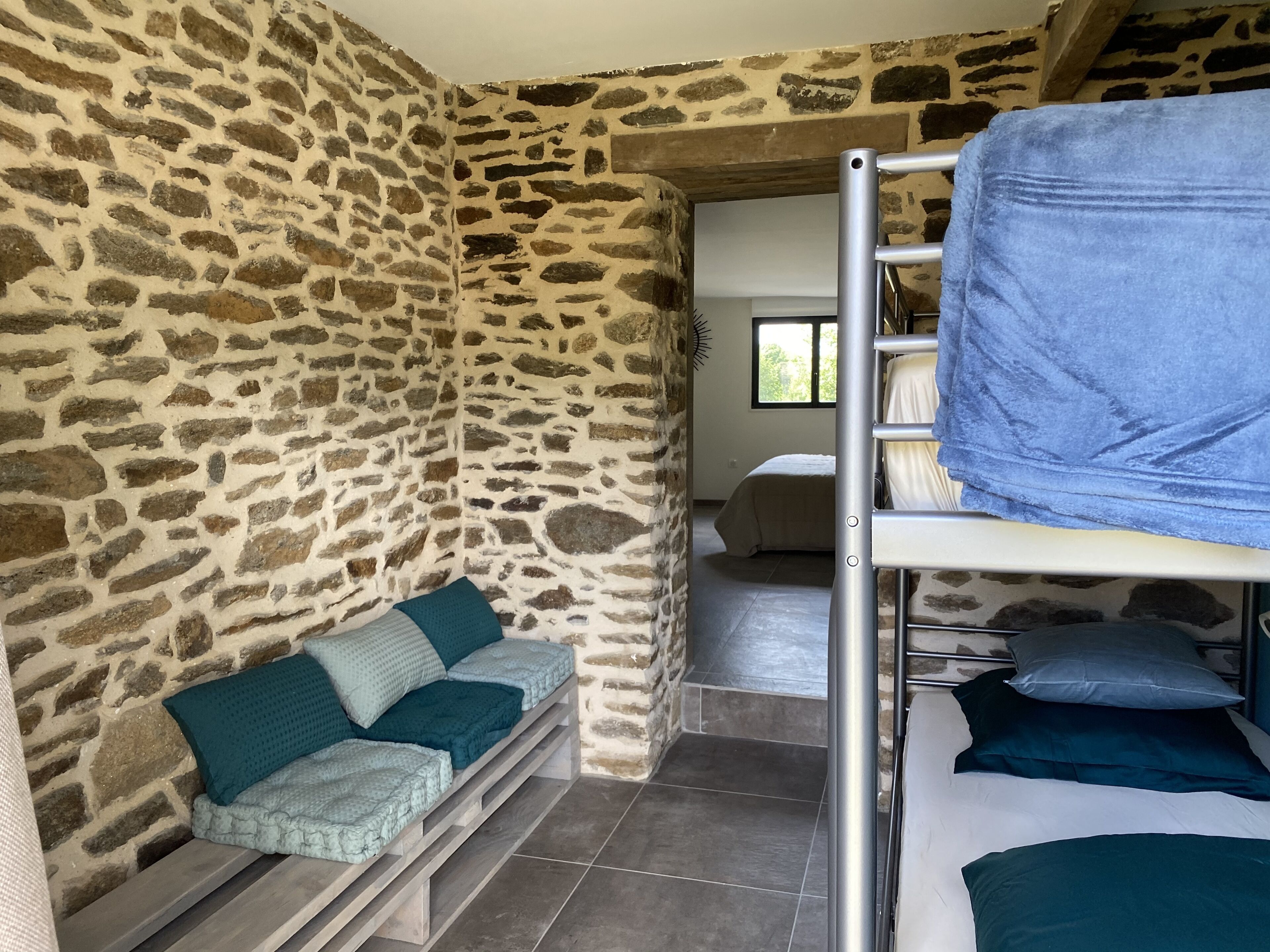 A room with stone walls, a bunk bed, and a sofa with cushions.