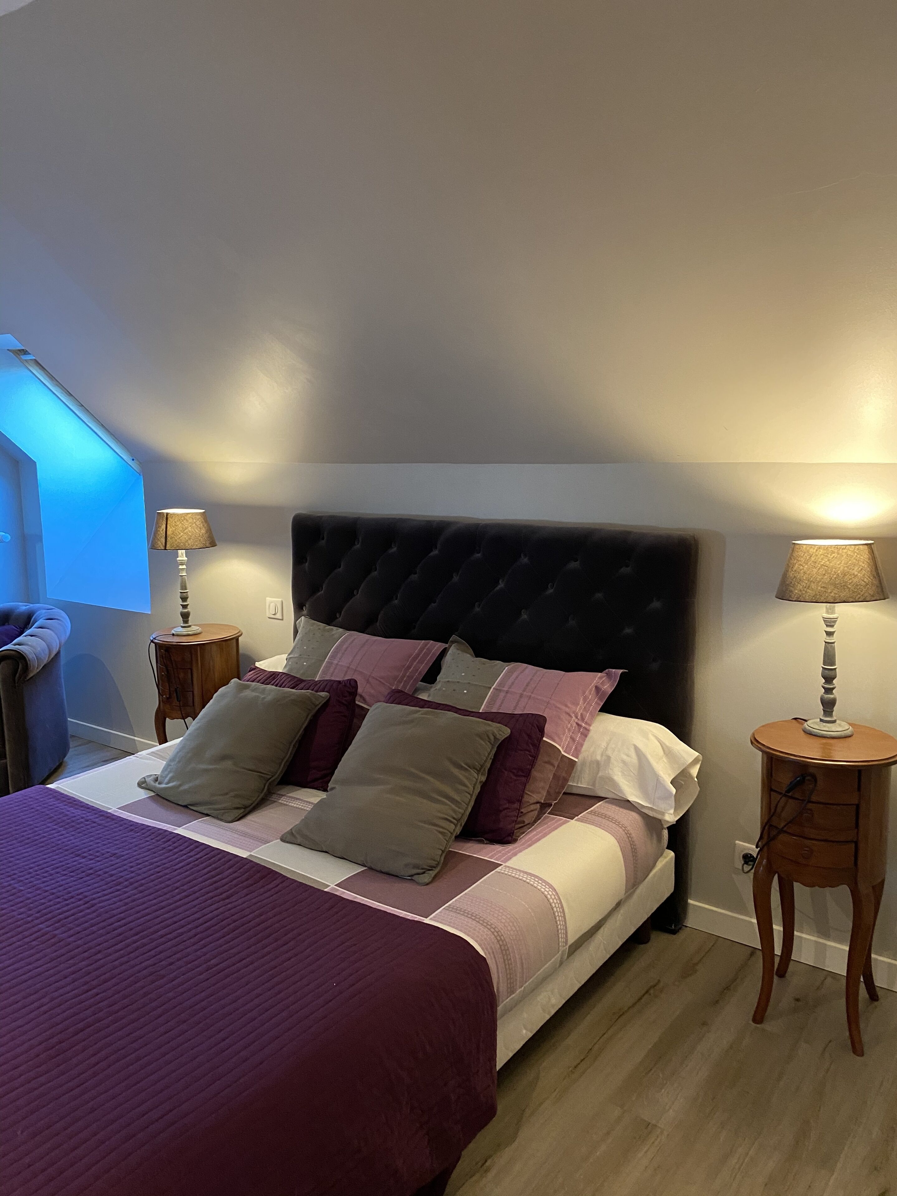 A neatly made bed with a dark headboard, two bedside tables with lamps, and a window with blinds.