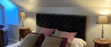 A neatly made bed with a dark headboard, two bedside tables with lamps, and a window with blinds.