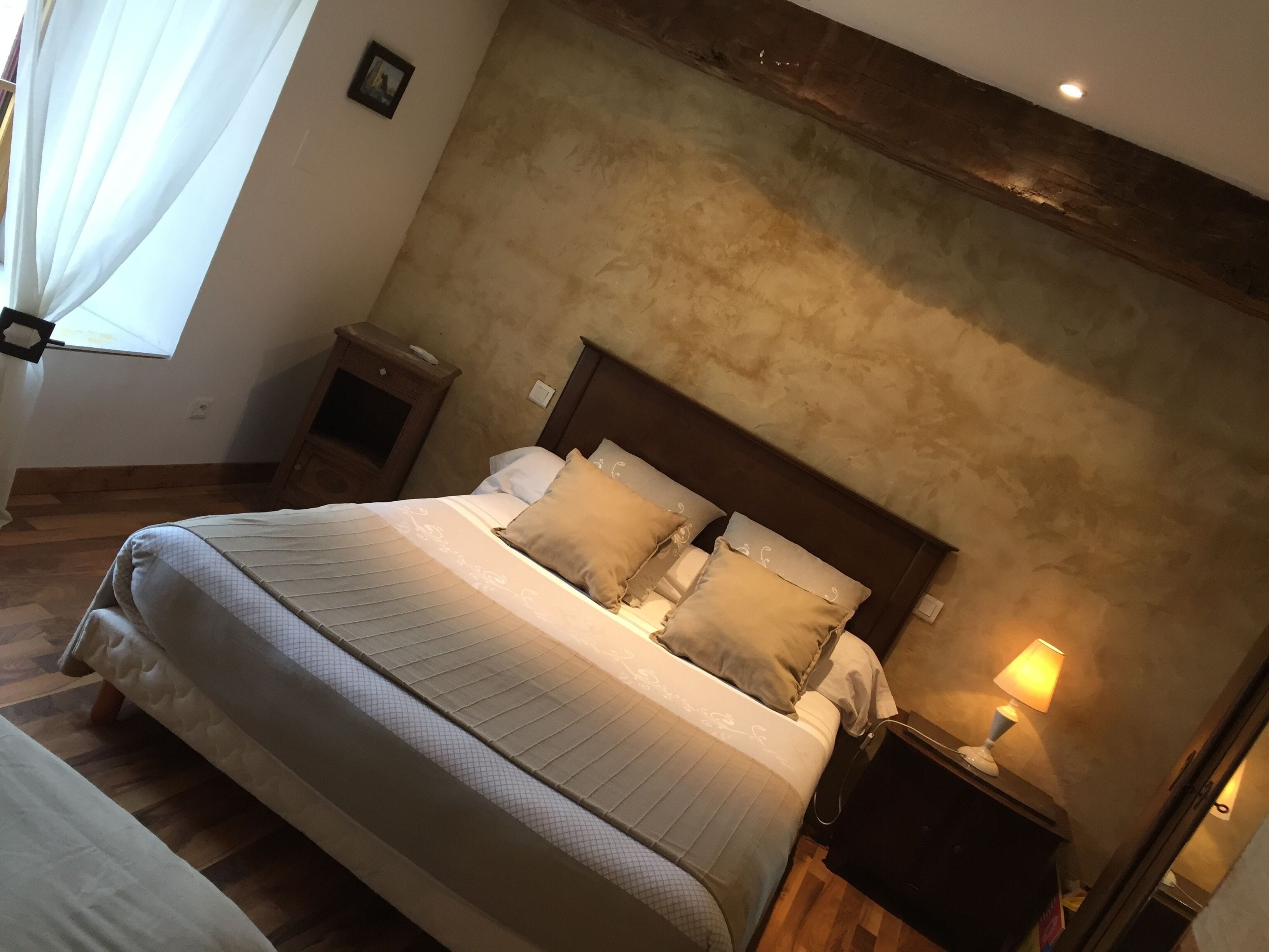 Una cama bien hecha con cabecera, una mesita de noche con lámpara y un pequeño atril.