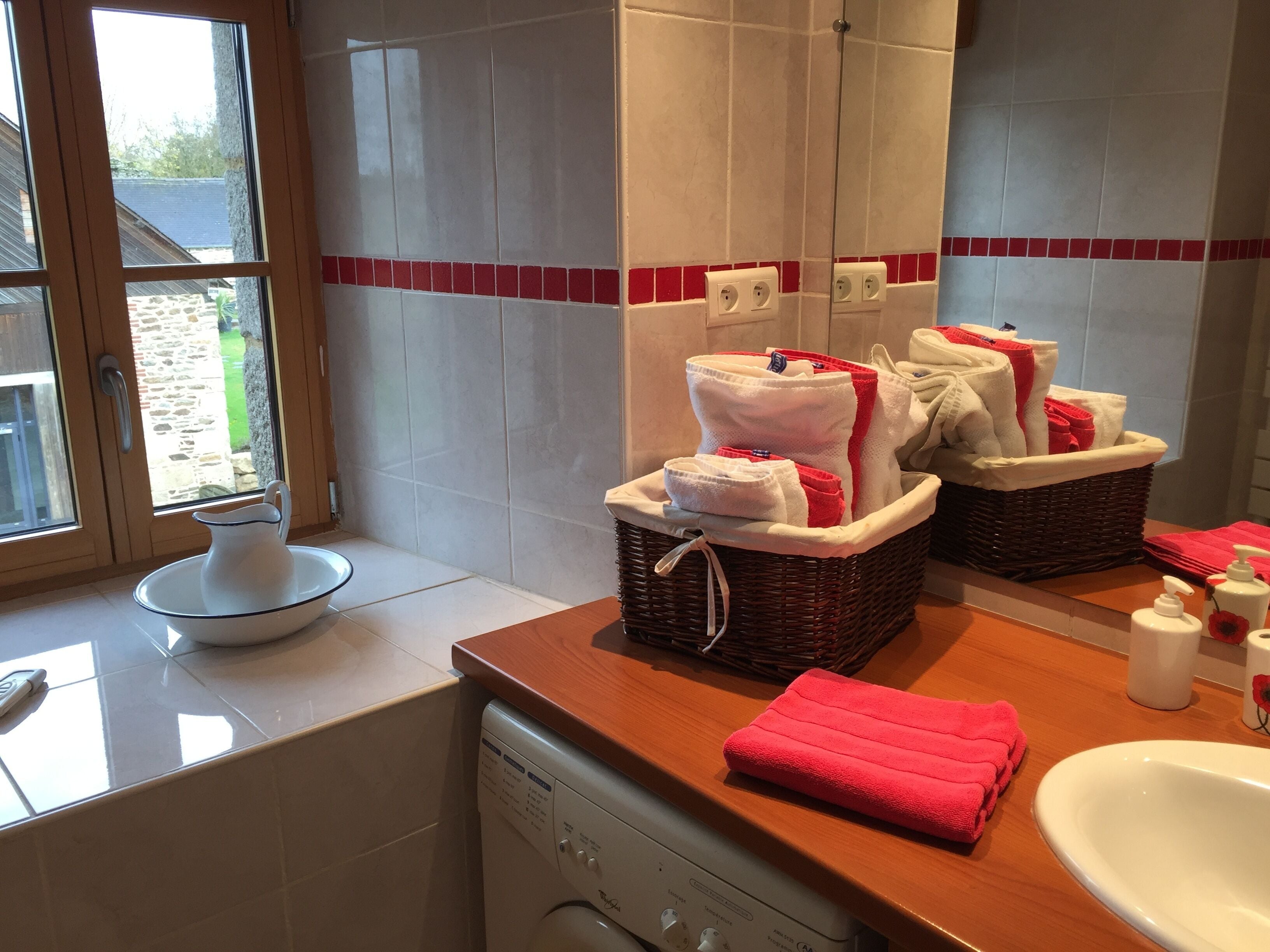 Une salle de bain avec un plan de toilette en bois, un lavabo et un lave-linge. On y trouve des serviettes et des articles de toilette sur le plan de toilette.