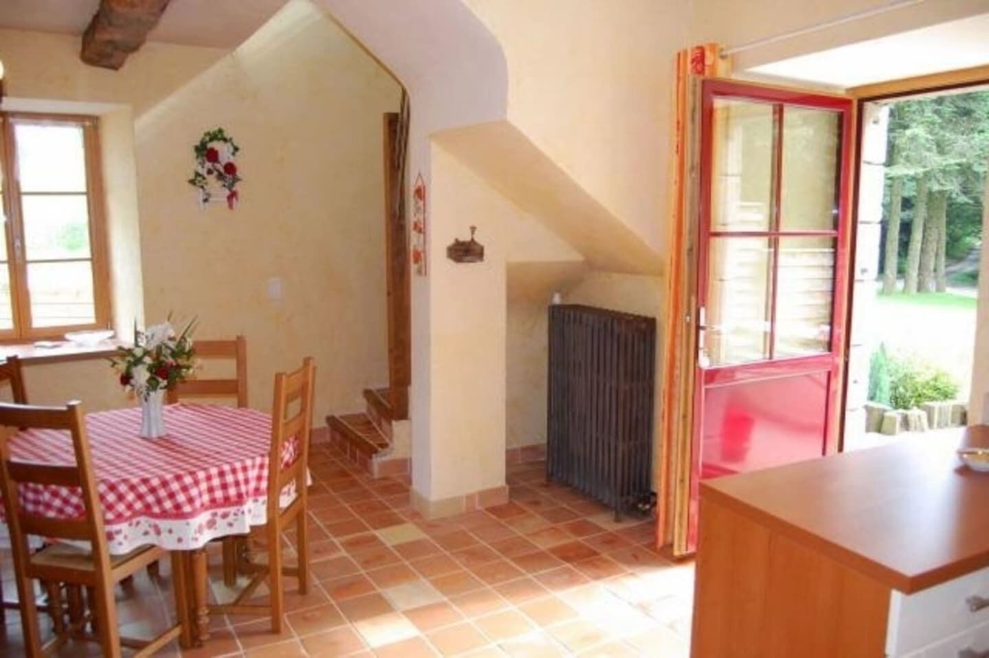 Un coin repas avec une table dressée pour deux personnes, un escalier et une porte à cadre rouge donnant sur l’extérieur.
