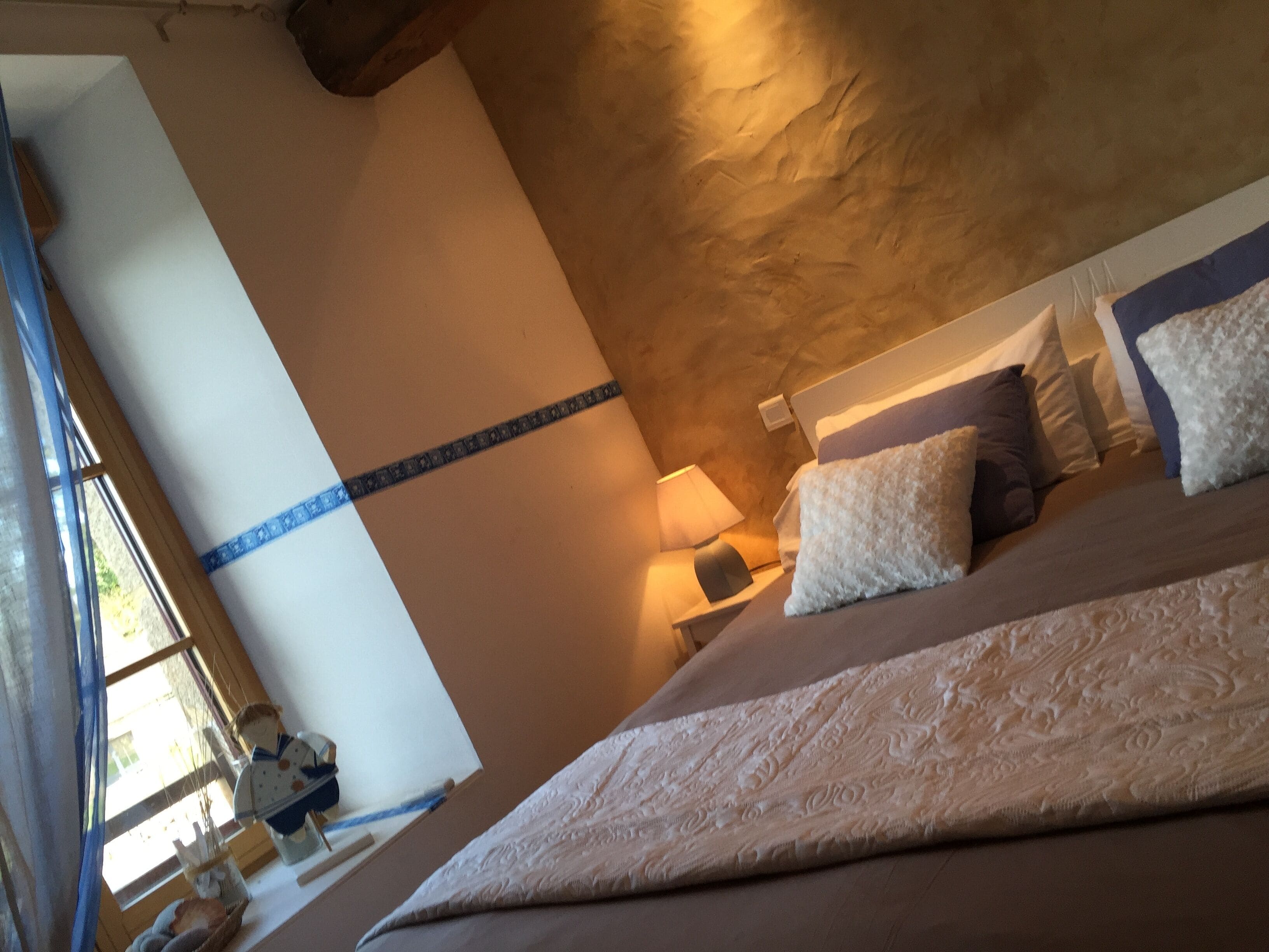 A bedroom with a large bed, a nightstand, a lamp, and a window with curtains.