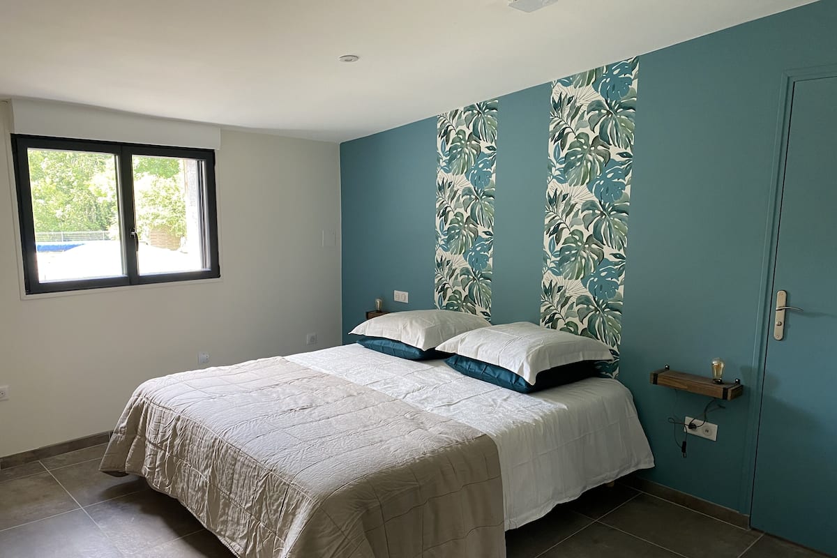 A bedroom with a bed, a window, and a wall with a tropical leaf pattern.